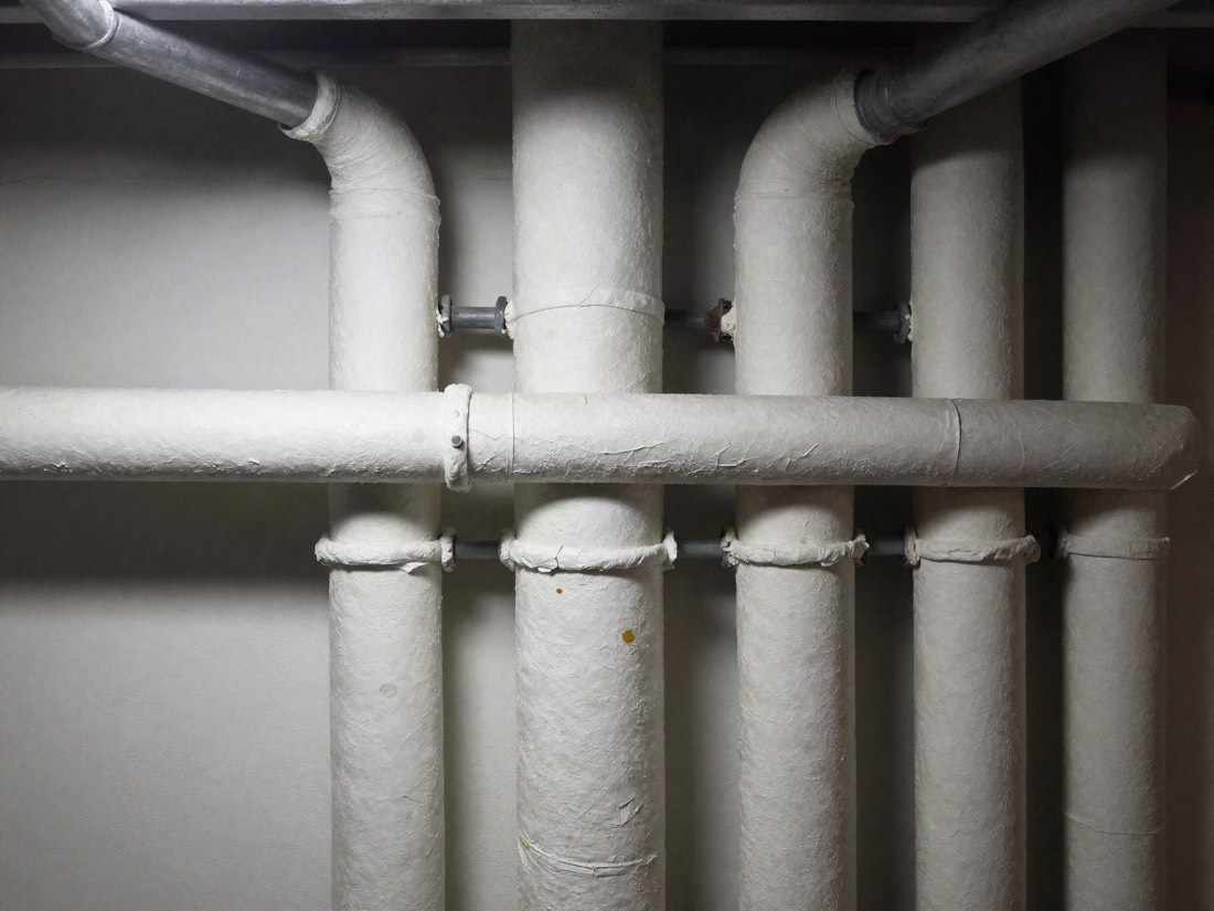 Cracked white thermal lagging wrapped around basement pipework