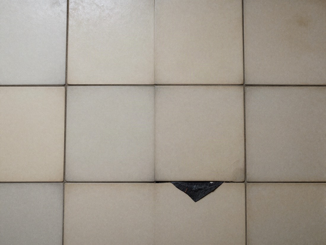 Worn vinyl floor tiles with bitumen adhesive visible at a lifted corner